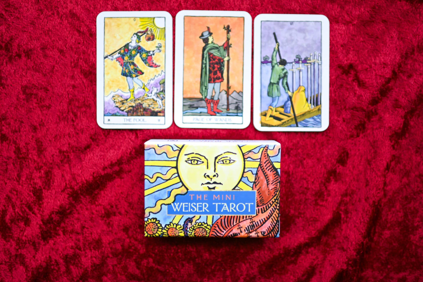 Three tarot cards on a red fabric background with a box labeled 'The Mini Weiser Tarot'.