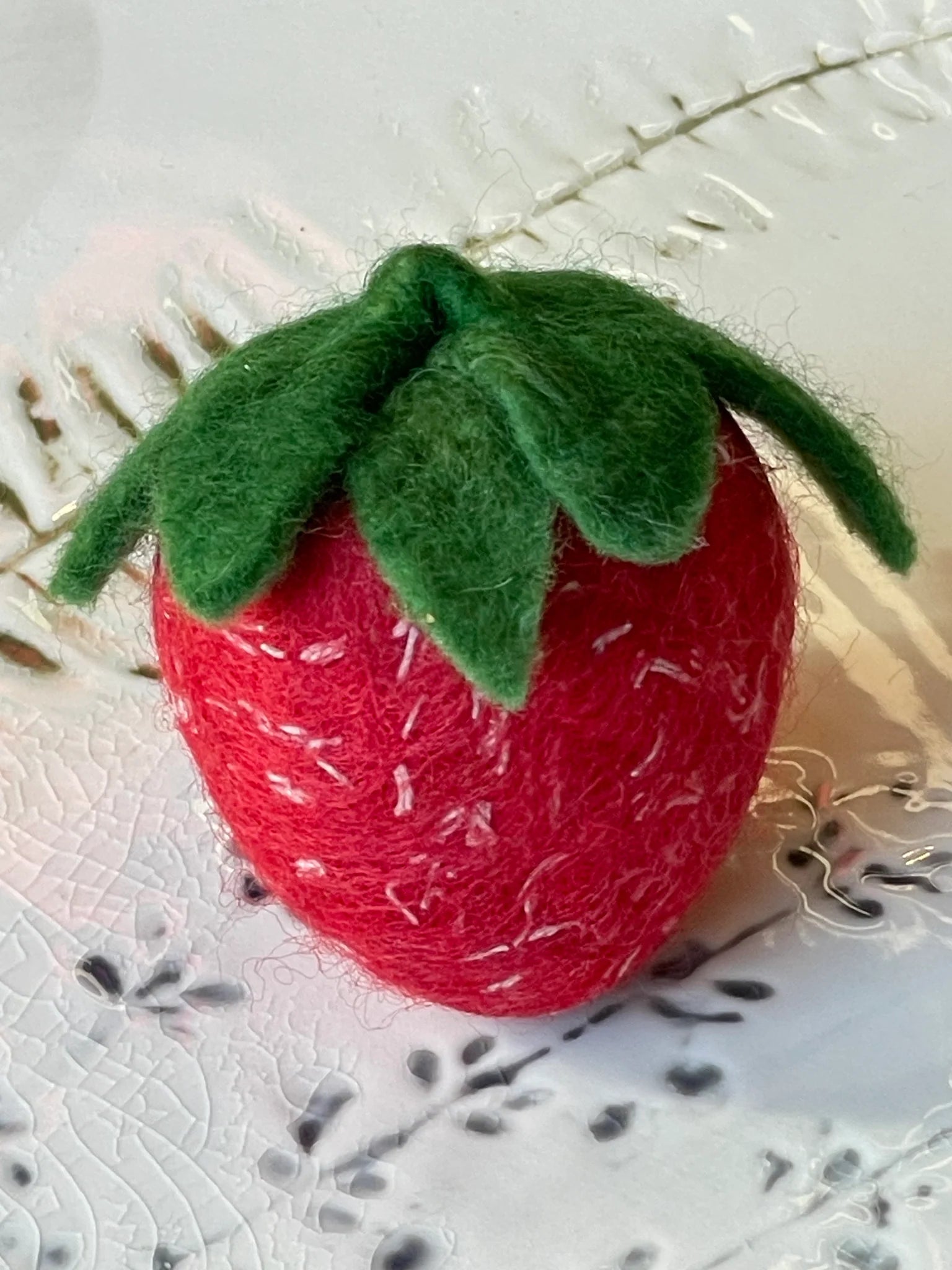 Red felt strawberry soap with green leaves on a textured white background