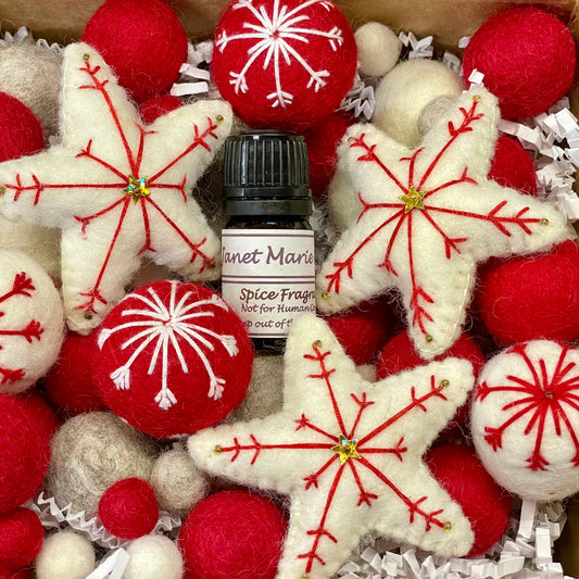 Small bottle of Janet Marie spice fragrance surrounded by red and white decorative stars and balls.